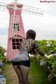 A woman in a black dress standing in front of a pink windmill.