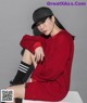 A woman sitting on top of a white box wearing a red dress and a black hat.