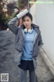 A woman in a gray jacket and blue shirt holding a water bottle.