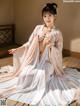 A woman in a white and pink kimono sitting on a wooden floor.