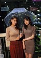 Two young women standing next to each other holding an umbrella.