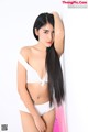 A woman in a white bikini leaning against a wall.