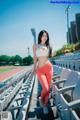 A woman in a white top and red leggings standing in a stadium.