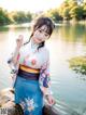 A woman in a blue and white kimono posing by a lake.