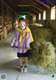 A woman in a school uniform holding a shovel in a barn.