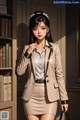 A woman in a beige suit standing in front of a bookcase.