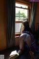 A woman sitting on a bed looking out a window.