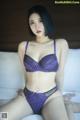 A woman in a purple lingerie sitting on a bed.