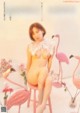 A naked woman sitting on a stool in front of pink flamingos.